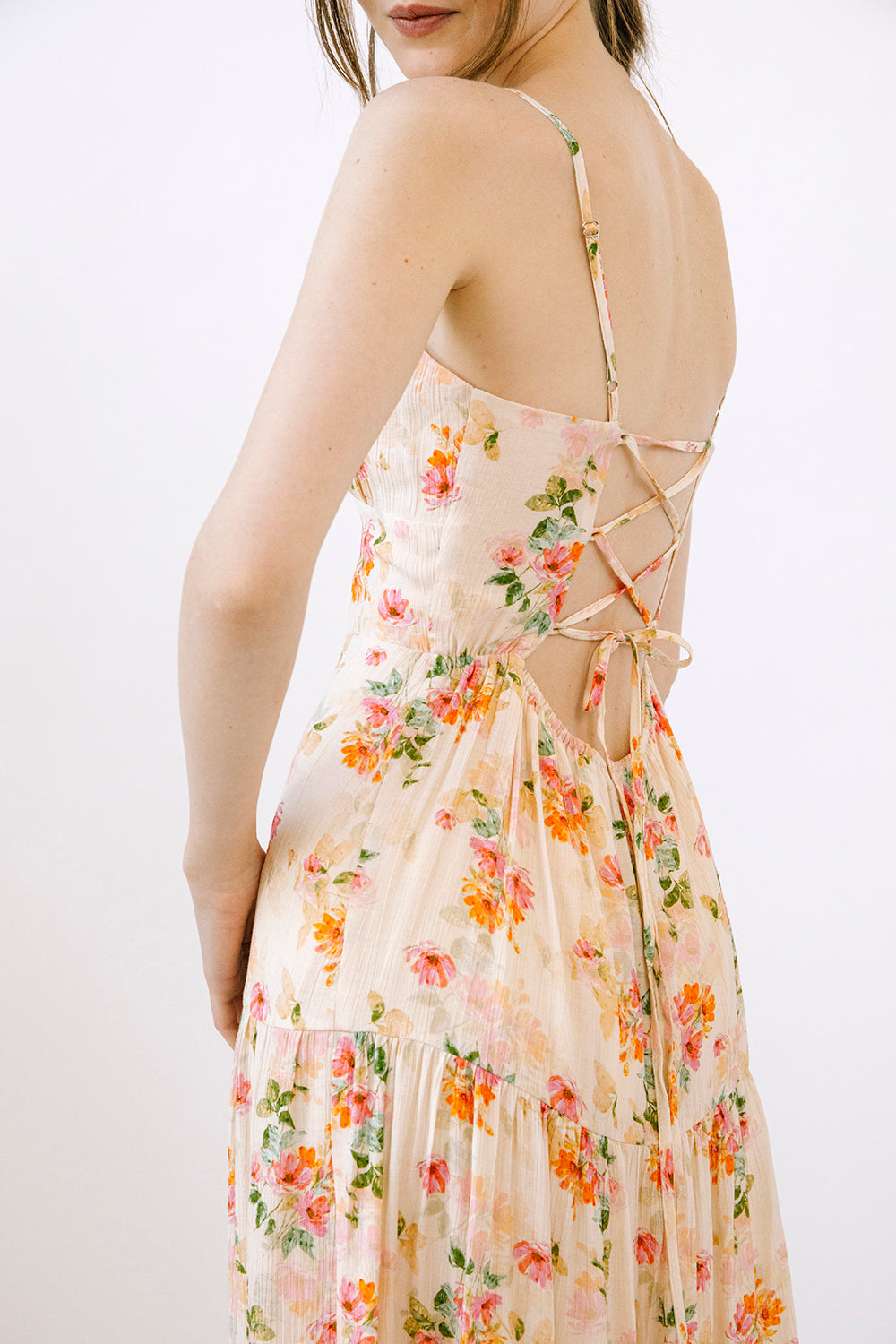 Woman wearing a cream dress with a floral pattern and an open back with a criss-cross adjustable tie