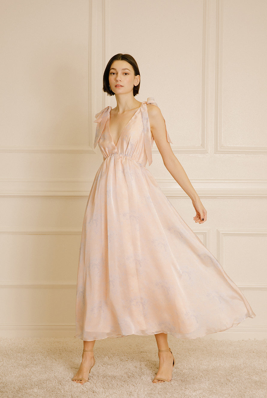 Modelo wearing a light pink dress with a v-neck against a neutral wall.