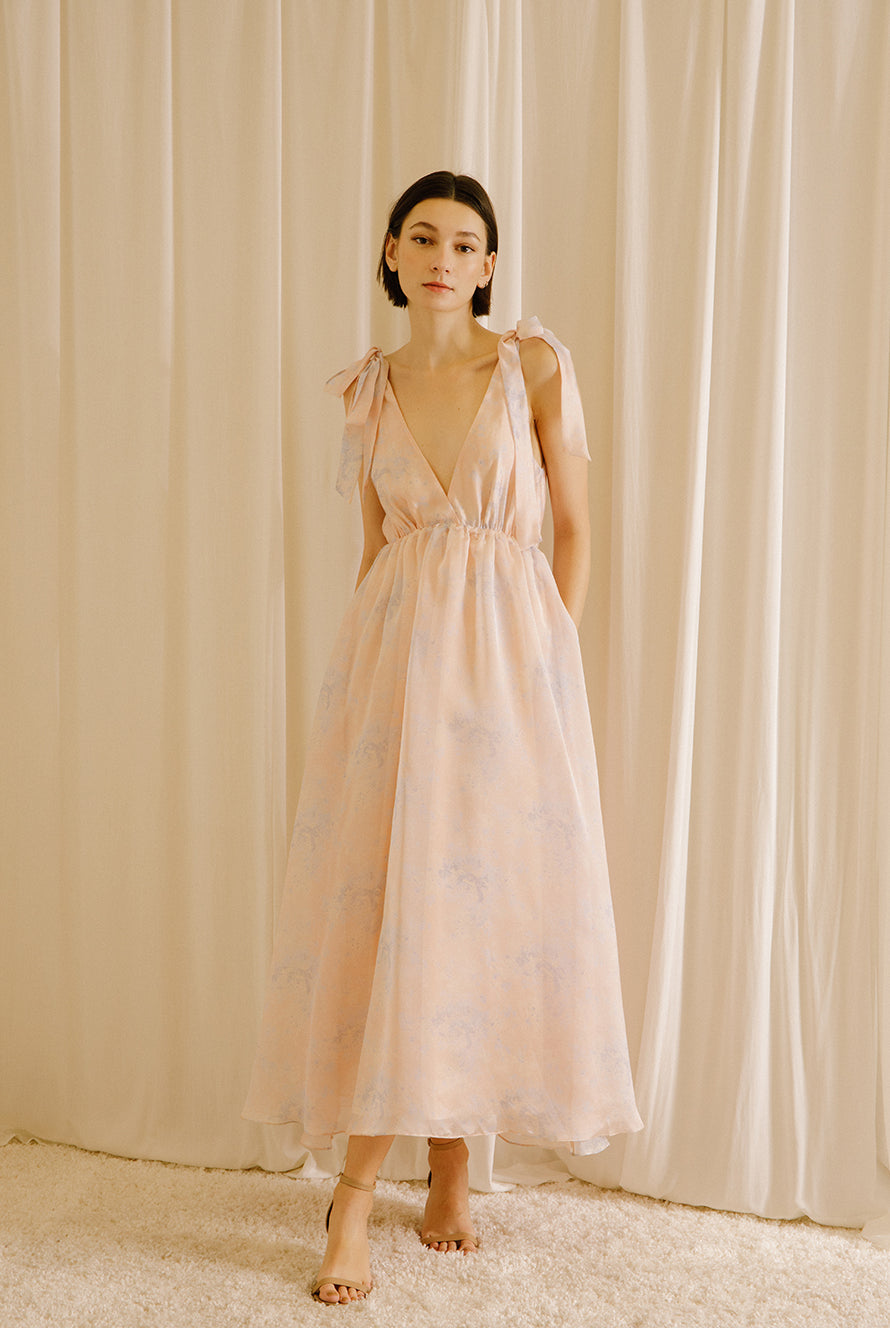 Woman wearing a light pink floral dress against a beige curtain background
