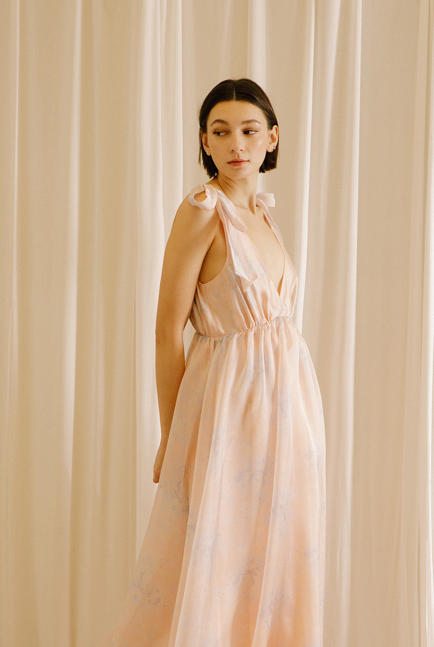 Side view of a woman wearing a light pink dress against a beige curtain background