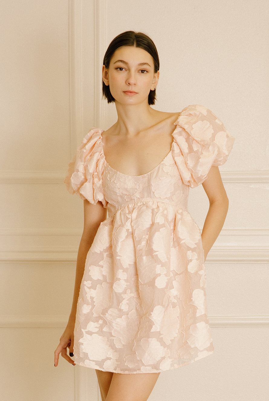 Woman wearing a peach dress against a neutral wall.