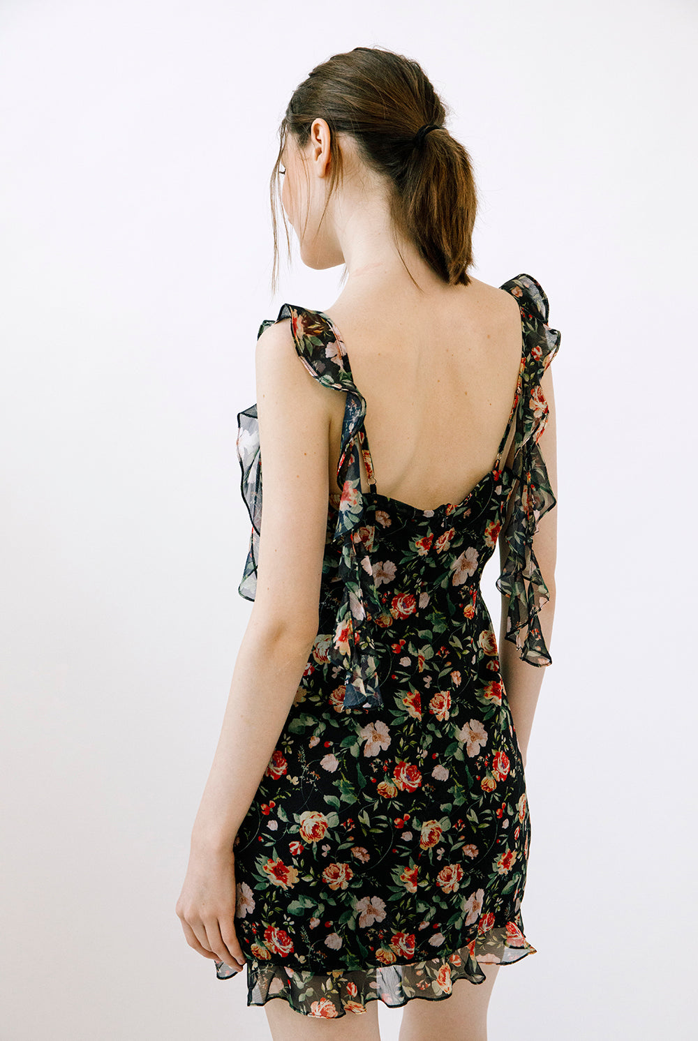 Woman wearing a floral dress with adjustable straps with ruffled details against a plain background