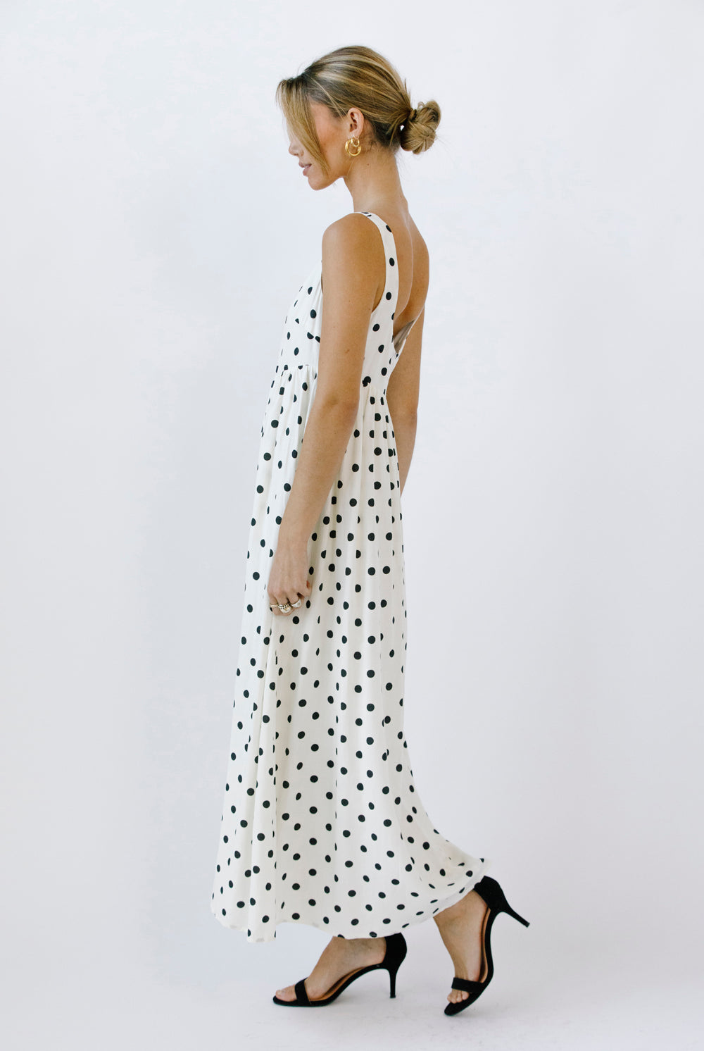Side view of a woman wearing a polka dot maxi dress on a white background