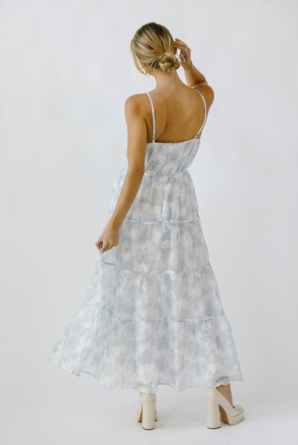 Back view of a woman wearing a light blue floral maxi dress on a white background