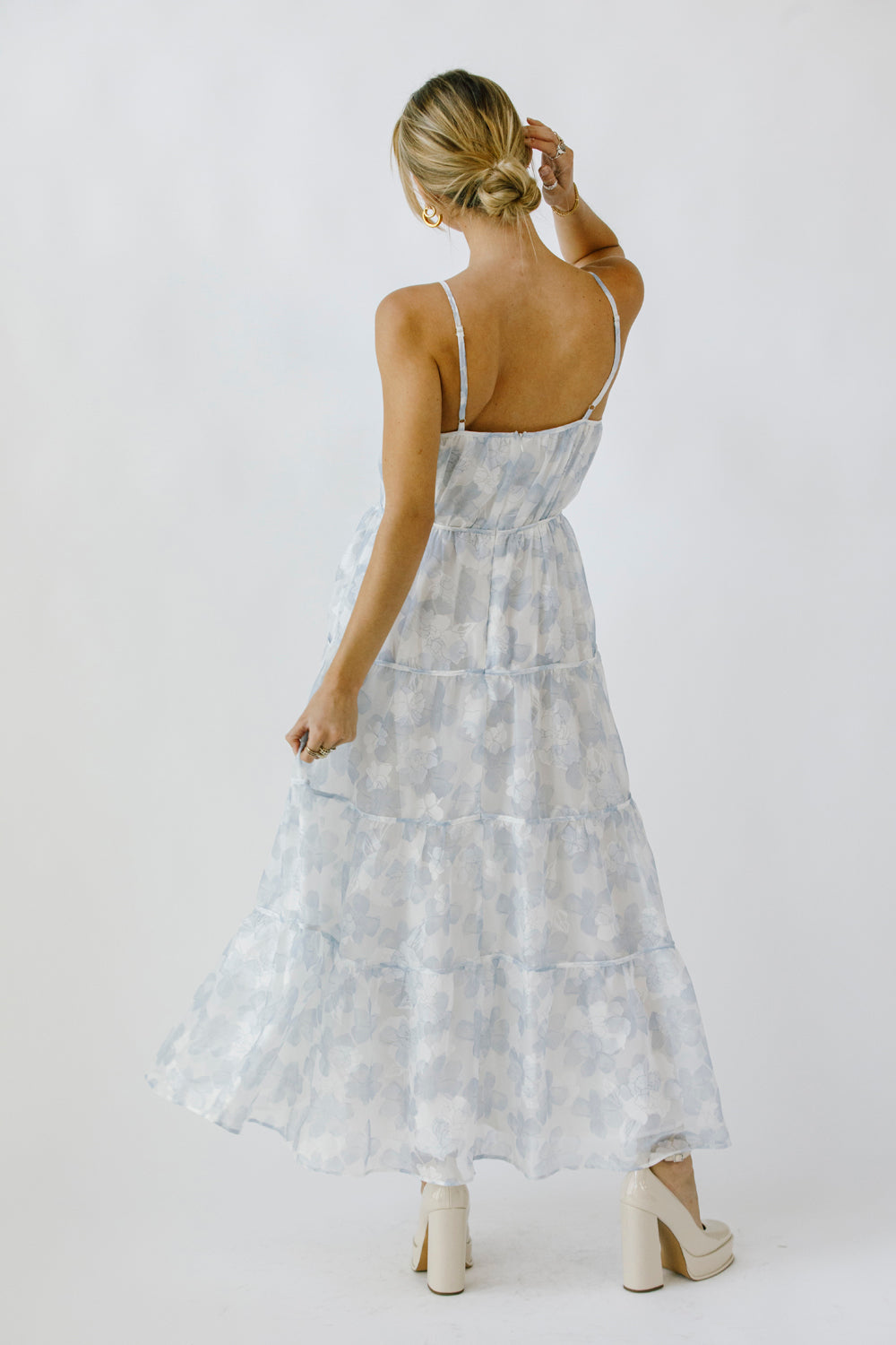 Back view of a woman wearing a light blue floral maxi dress on a white background