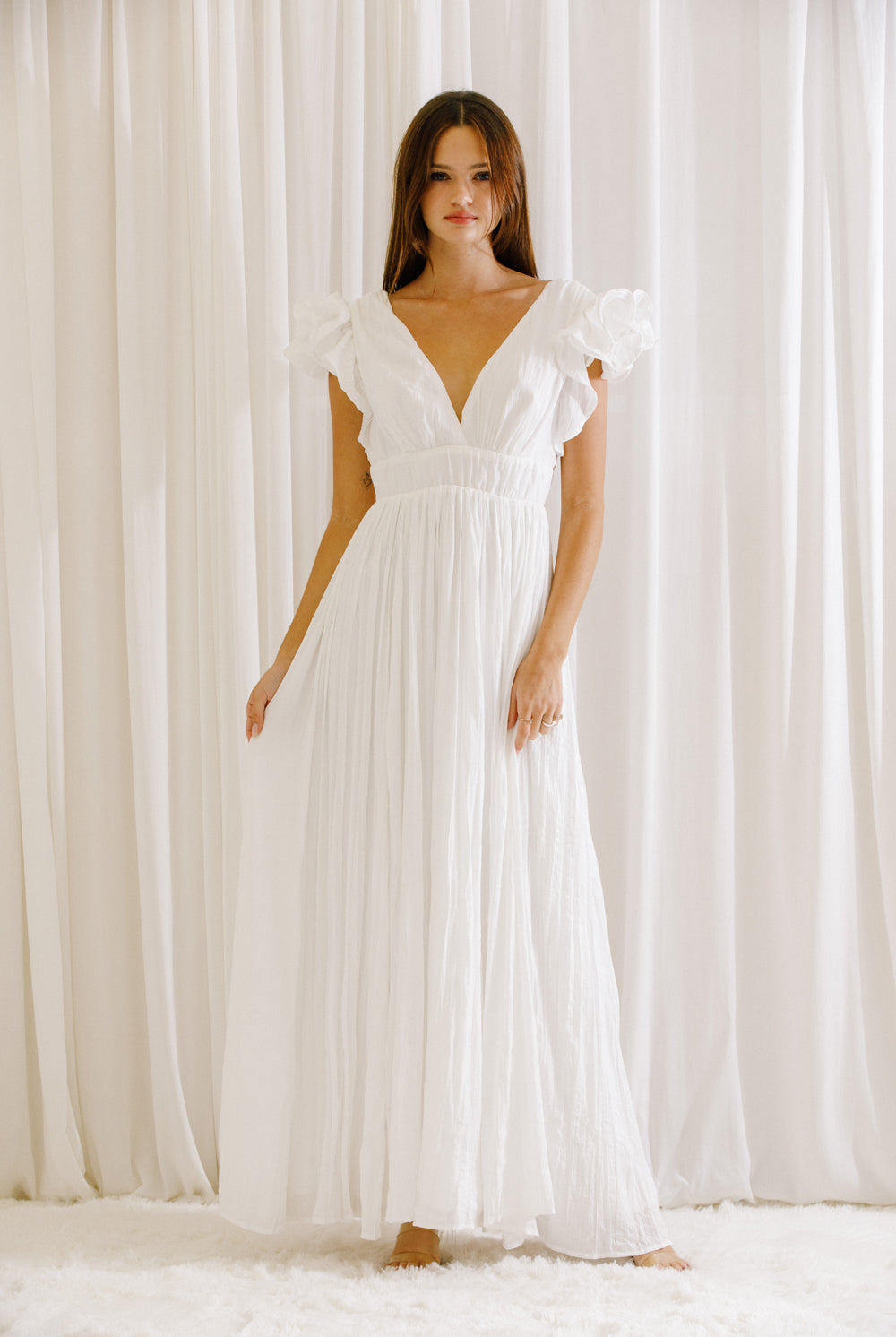 Woman wearing a white maxi dress standing against a white curtain