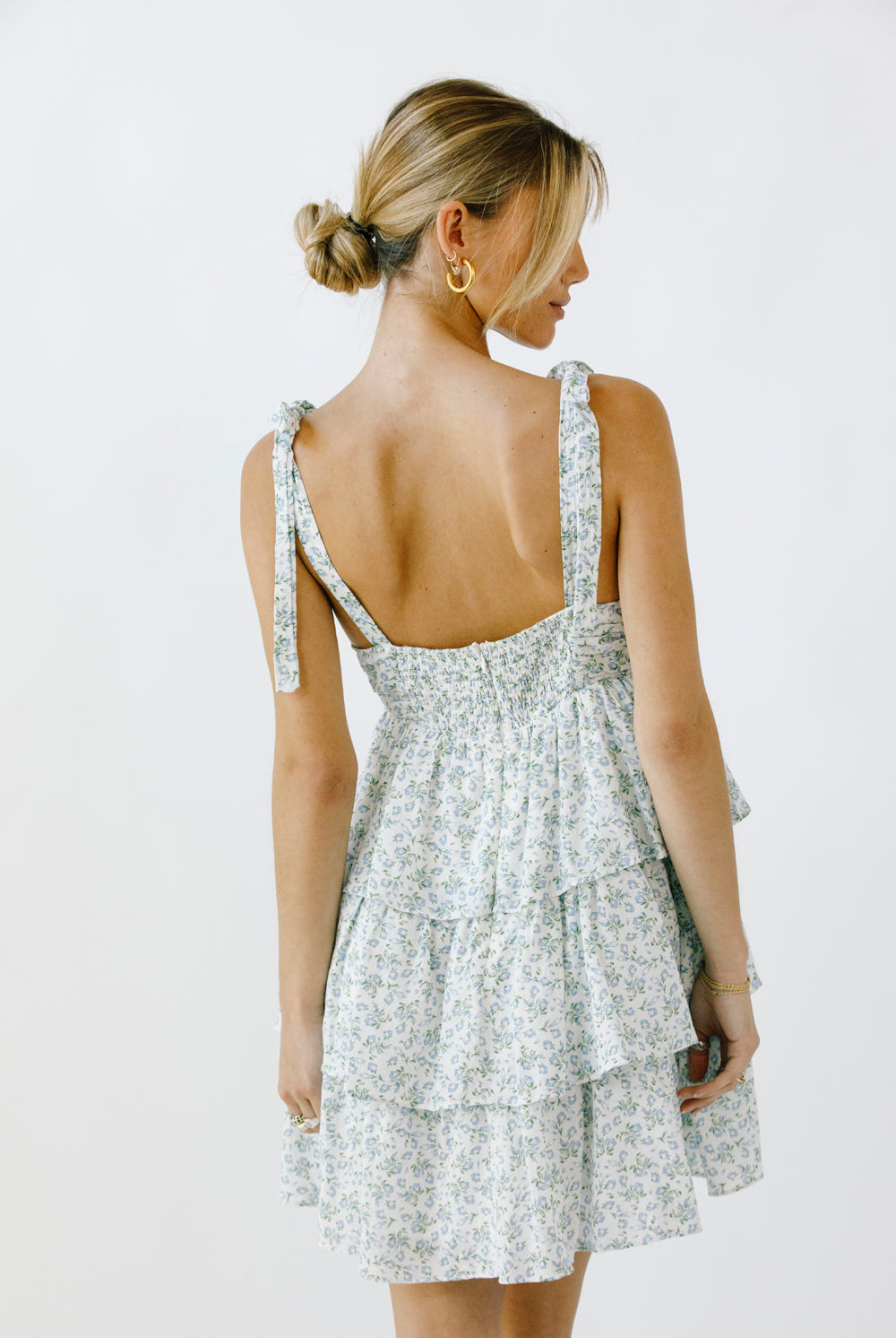 Back view of a woman wearing a floral dress with a tiered ruffle design on a white background
