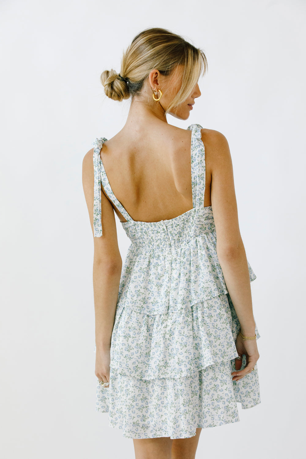 Back view of a woman wearing a floral dress with a tiered ruffle design on a white background