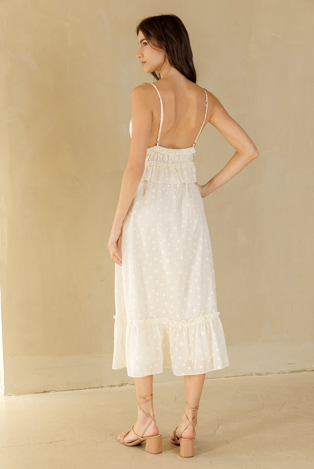 Back view of a woman wearing a cream midi dress against a beige background