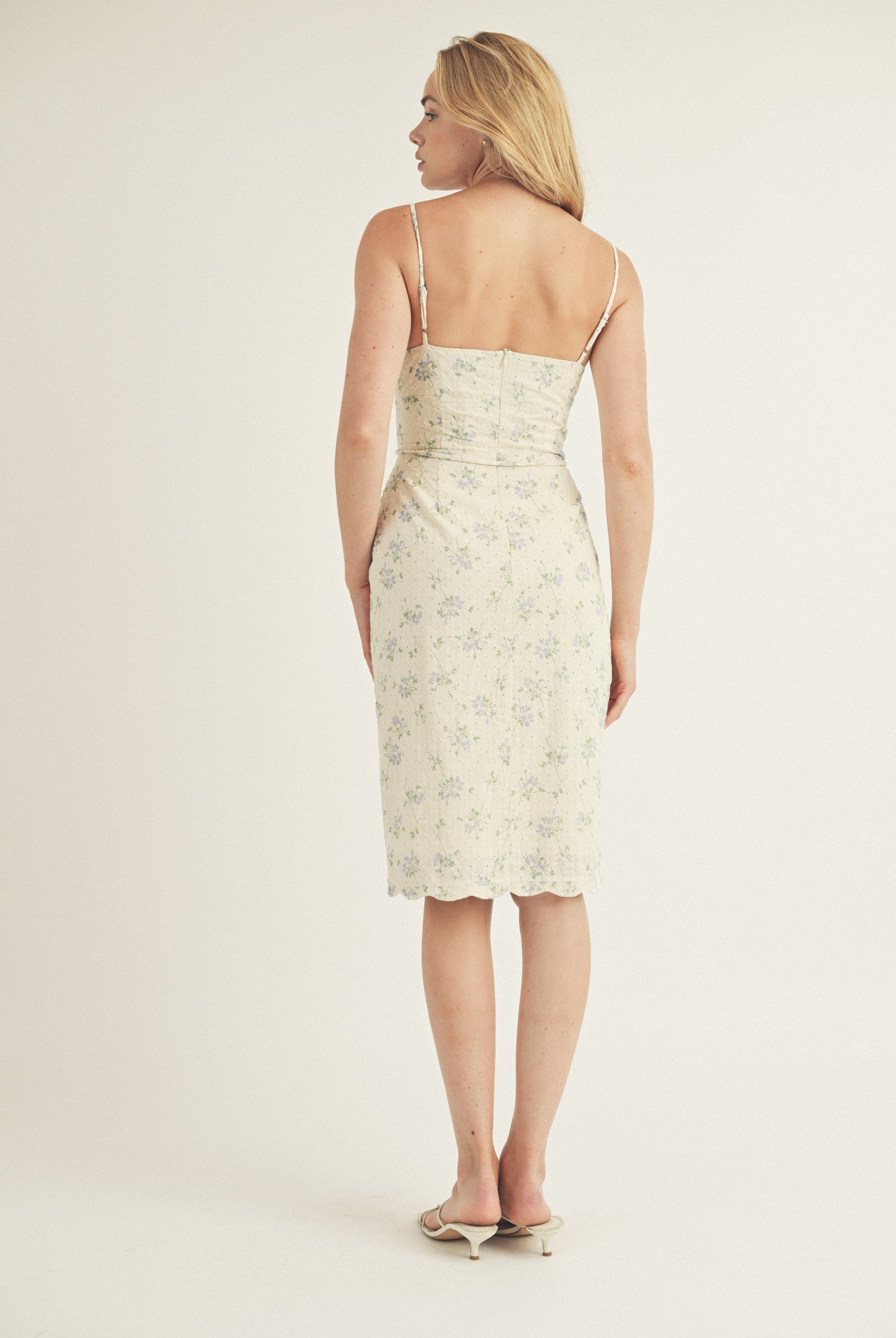 Back view of a woman wearing a floral slip dress on a plain background