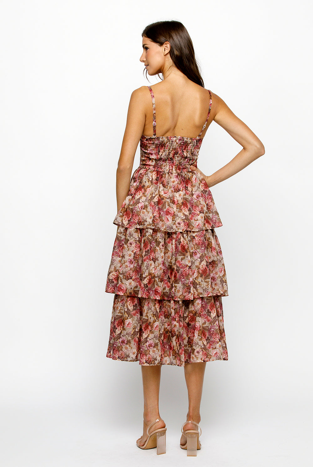 Back view of a woman wearing a floral tiered dress on a white background