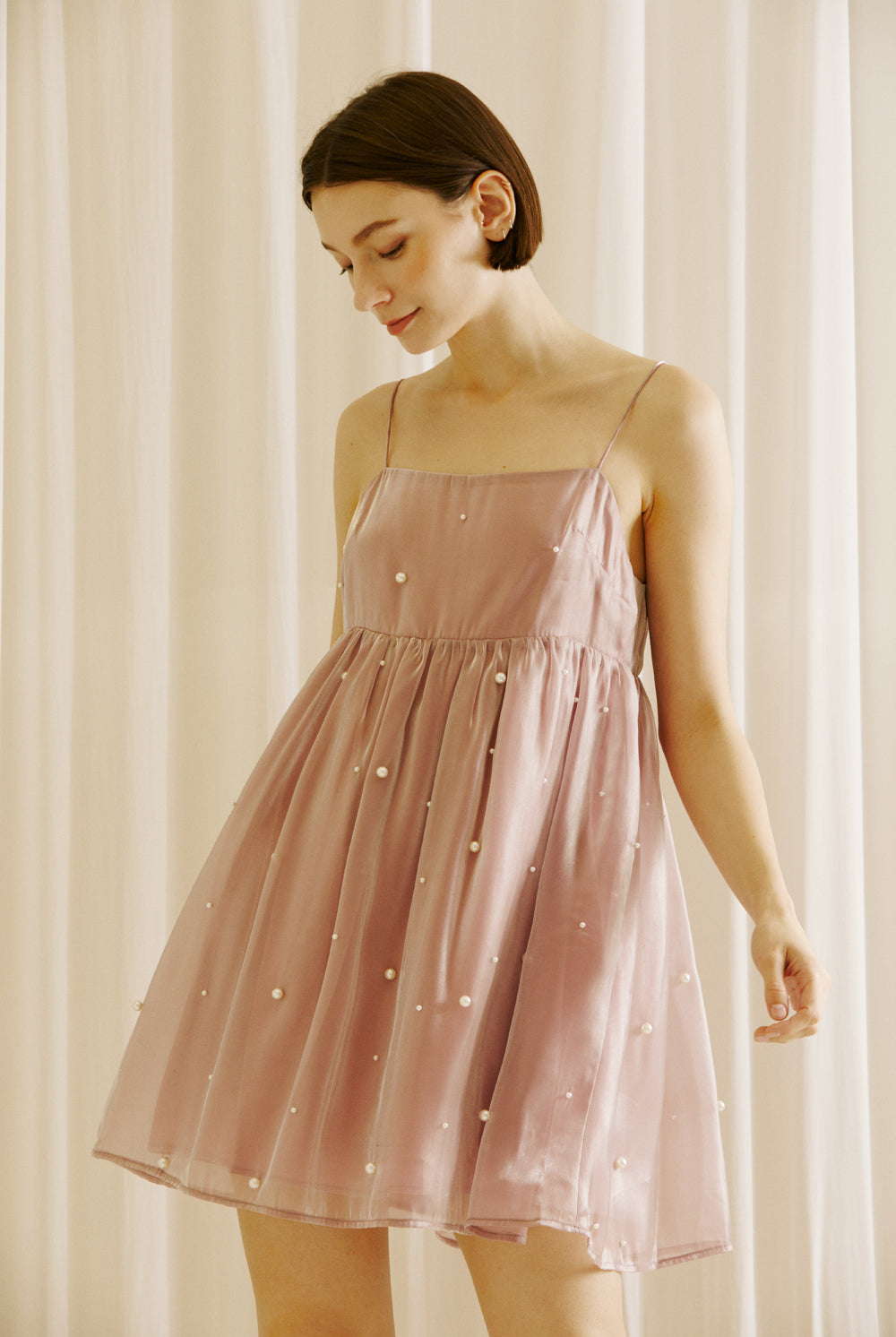 A model wears a mauve dress with pearl embellishments against a beige curtain background