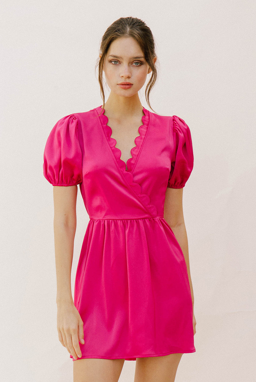Woman wearing a bright pink mini dress with puffed sleeves against a plain background