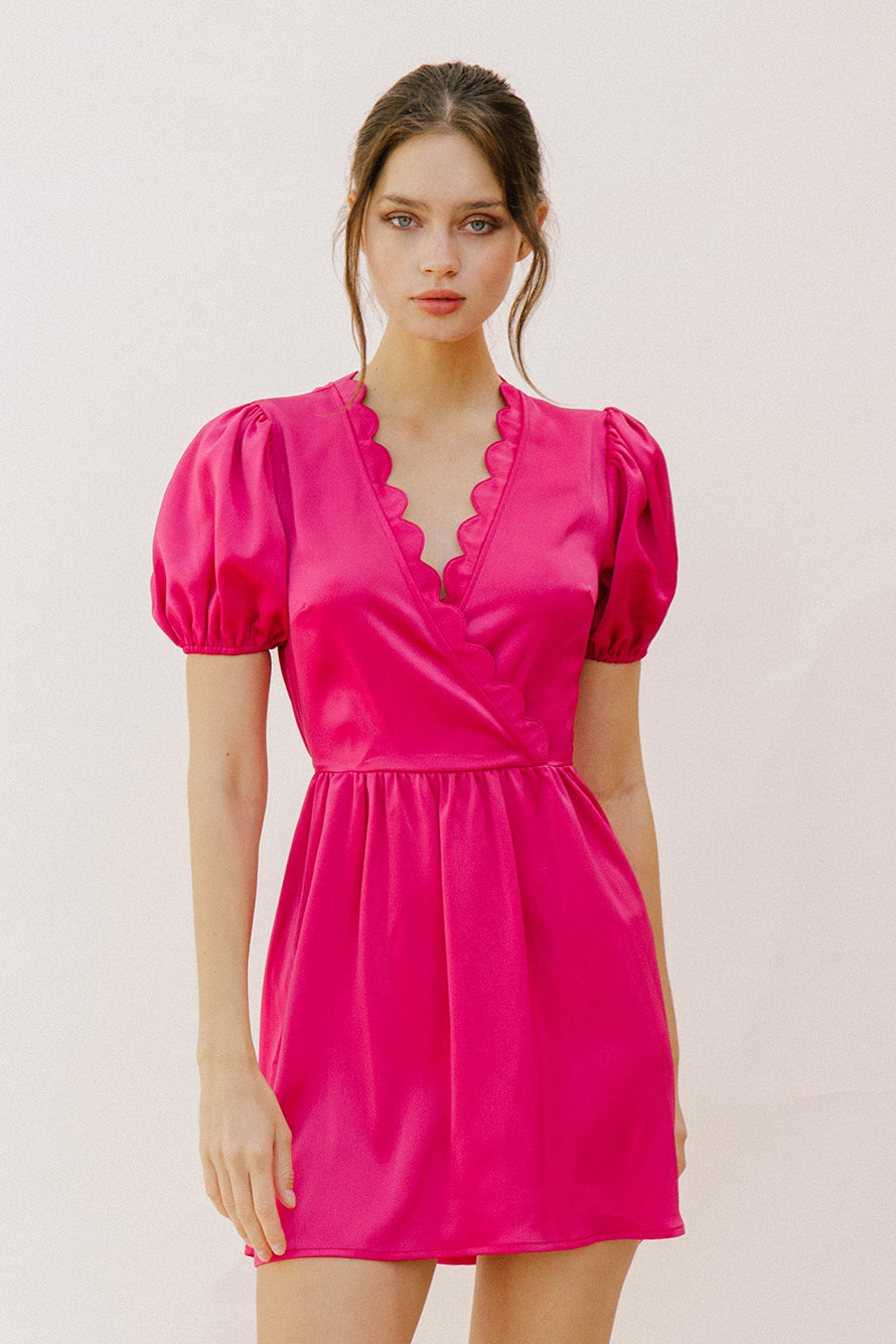 Woman wearing a bright pink mini dress with puffed sleeves against a plain background