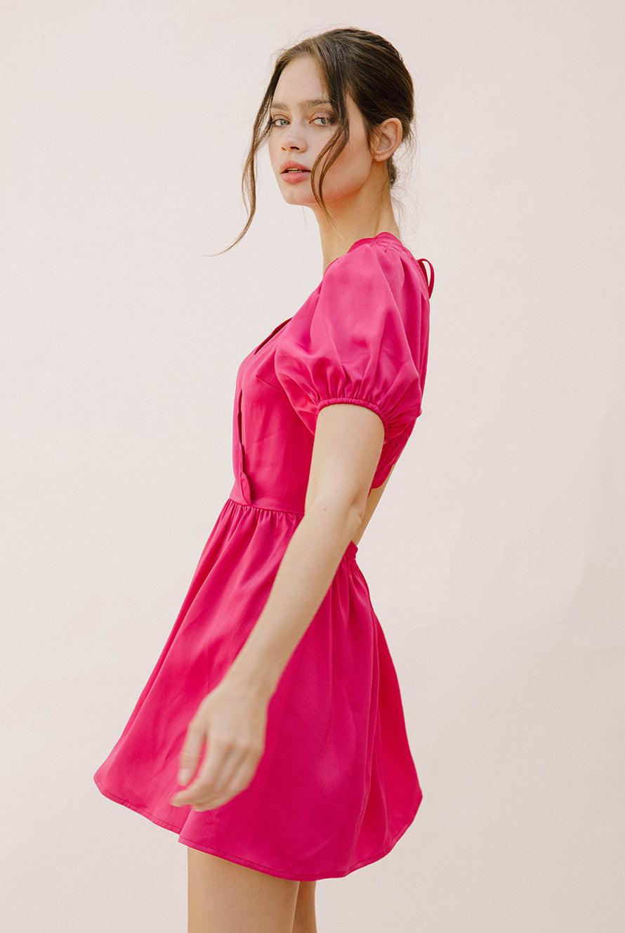 Side view of a woman wearing a bright pink mini dress with puffed sleeves against a plain background