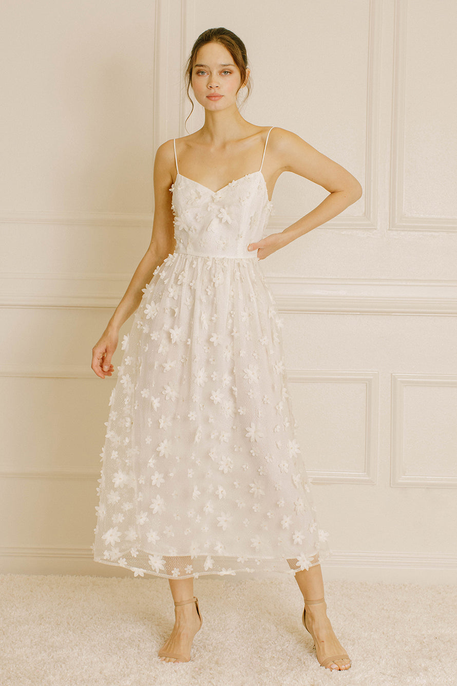 Woman wearing a white floral dress against a neutral wall.