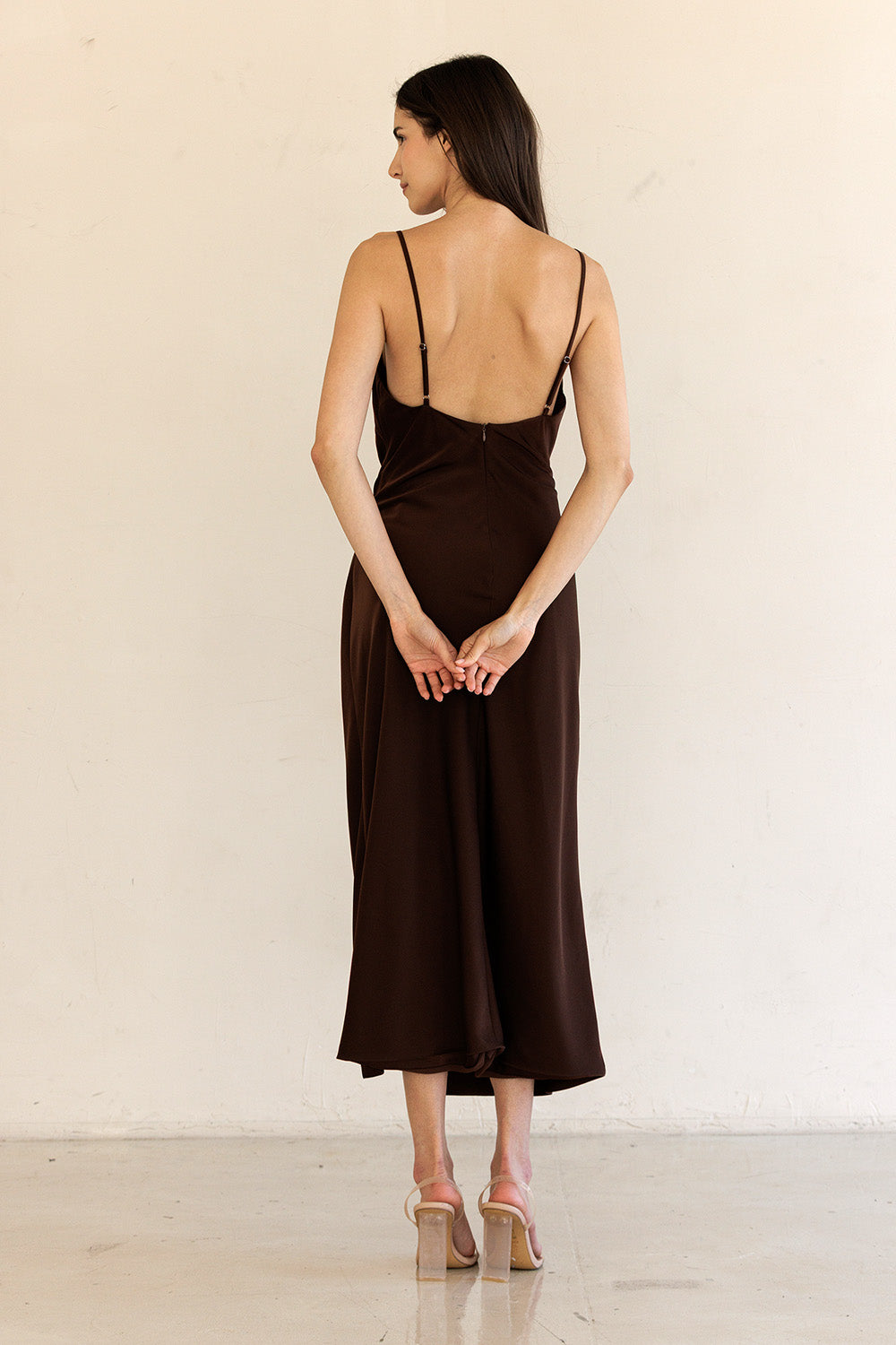 Back view of a woman wearing a brown slip dress against a white background