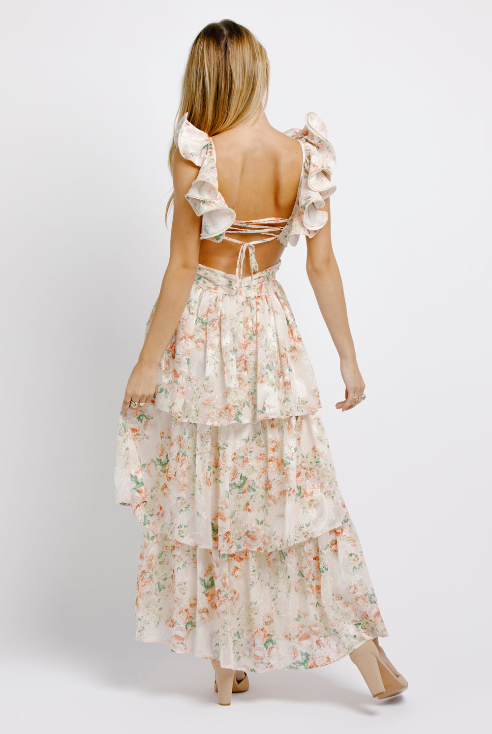 Back view of a woman wearing a cream floral maxi dress with ruffled sleeves on a white background