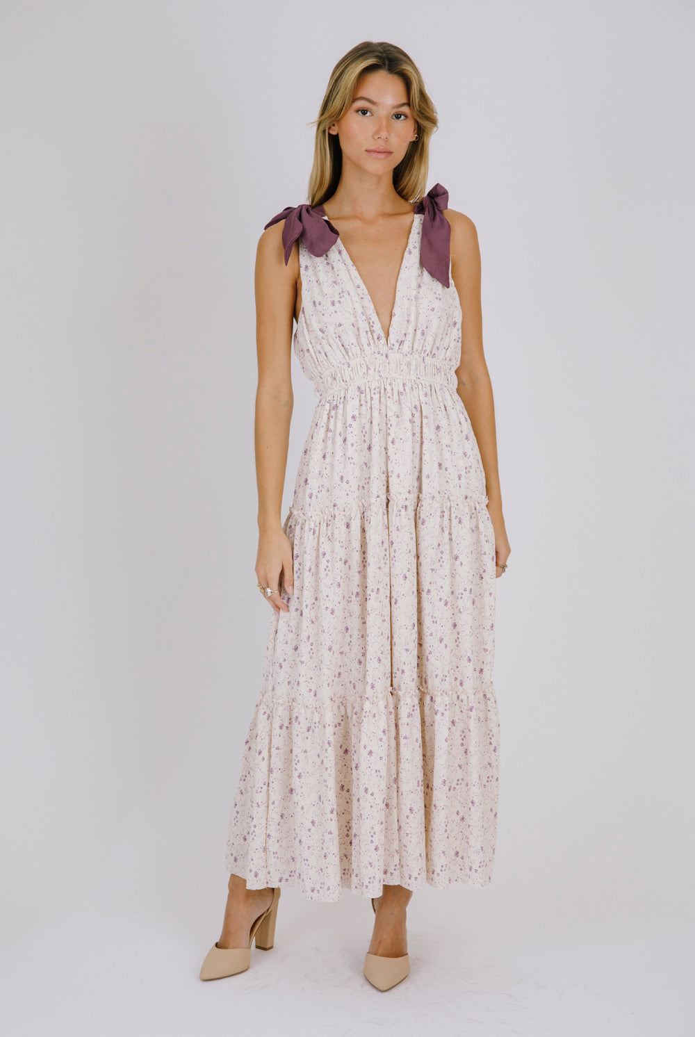 Woman wearing a purple floral maxi dress with bow straps details on a white background