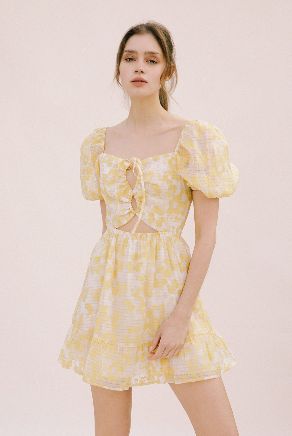 Woman wearing a yellow floral mini dress on a light pink background