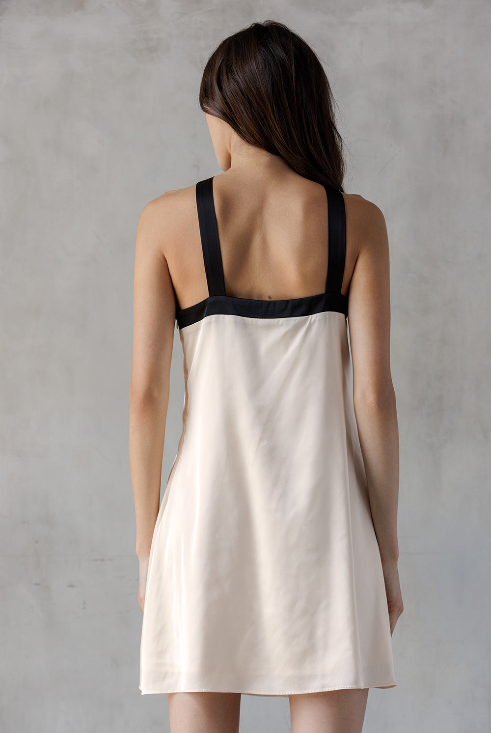Woman wearing a beige slip dress with black trim against a gray background
