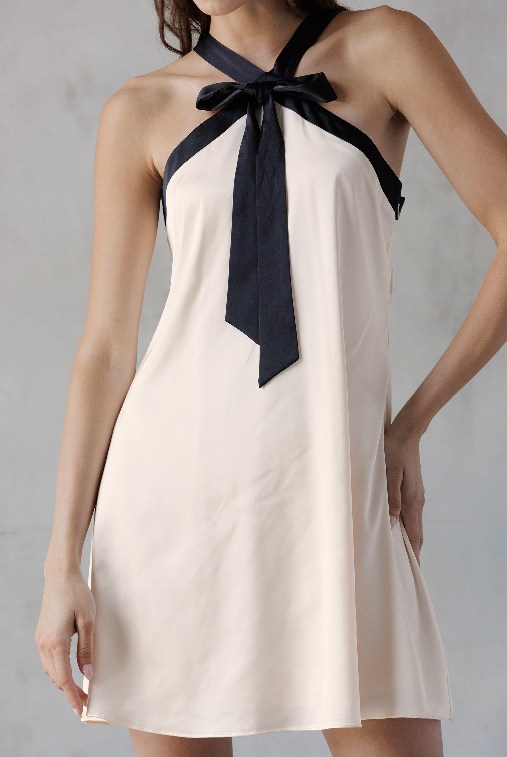 Beige halter dress with black ribbon tie on a gray background