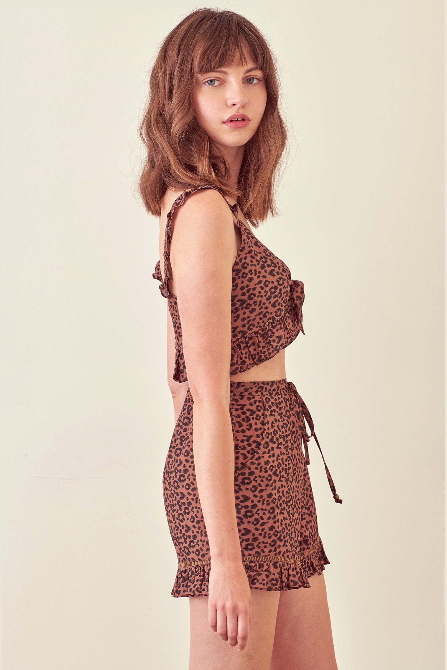 Side view of a woman wearing a leopard print cropped top and shorts on a beige background