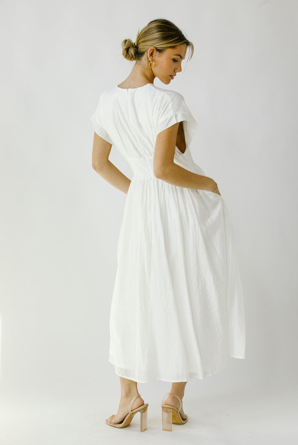 Back view of a woman wearing a white midi dress with an invisible zipper against a plain background