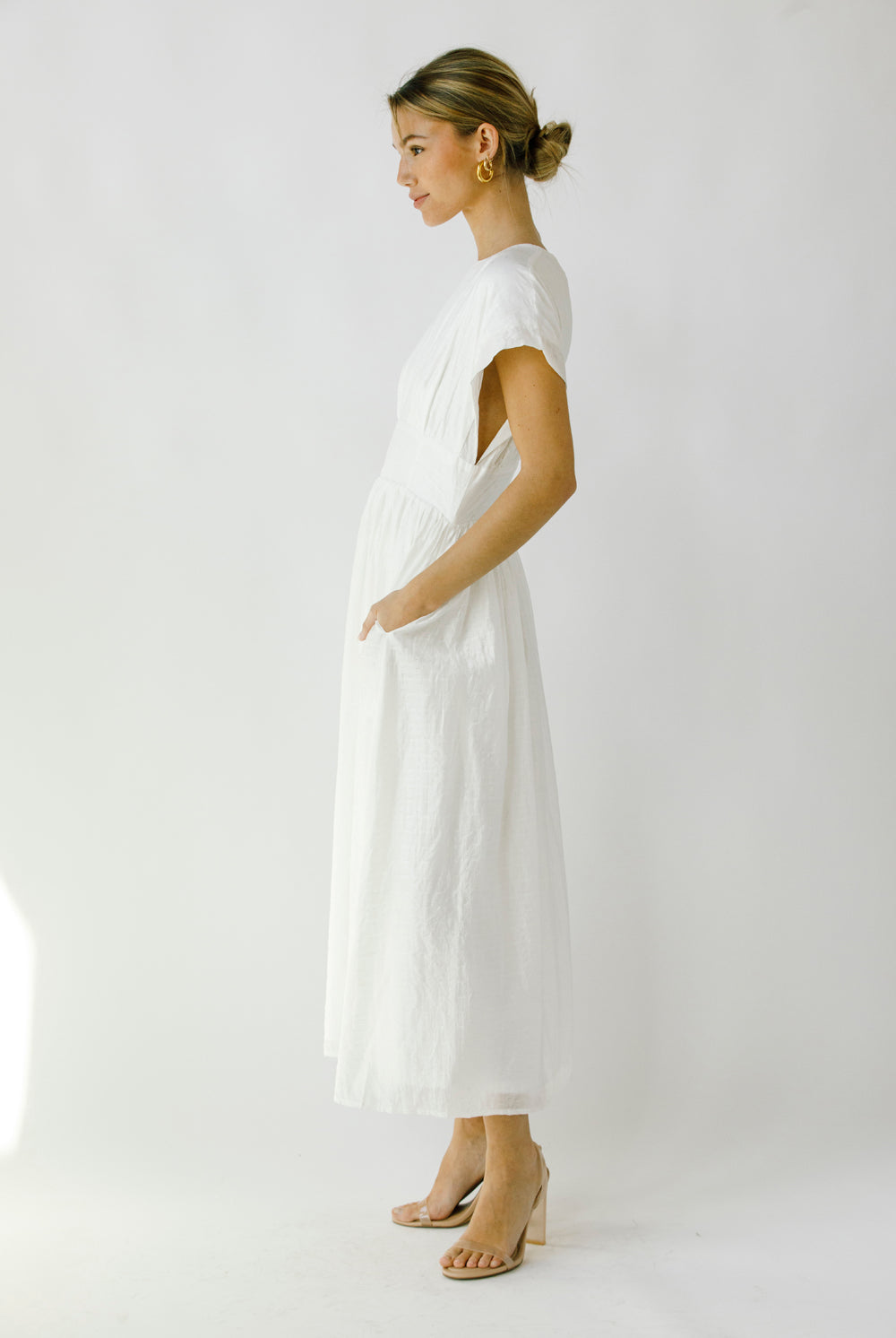 Side view of a woman wearing a white midi dress against a plain background