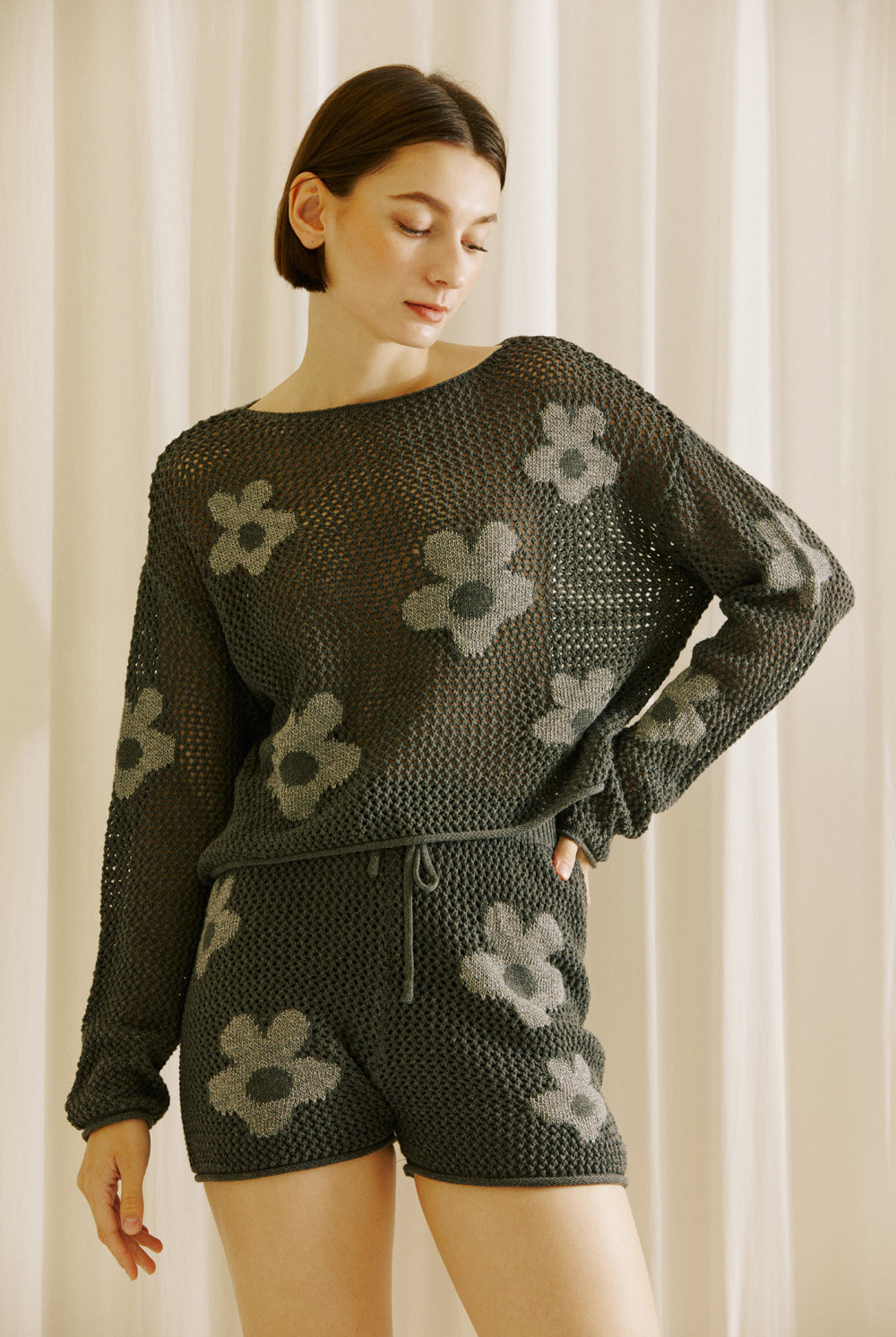 Woman wearing a dark grey crochet outfit with floral patterns against a neutral background