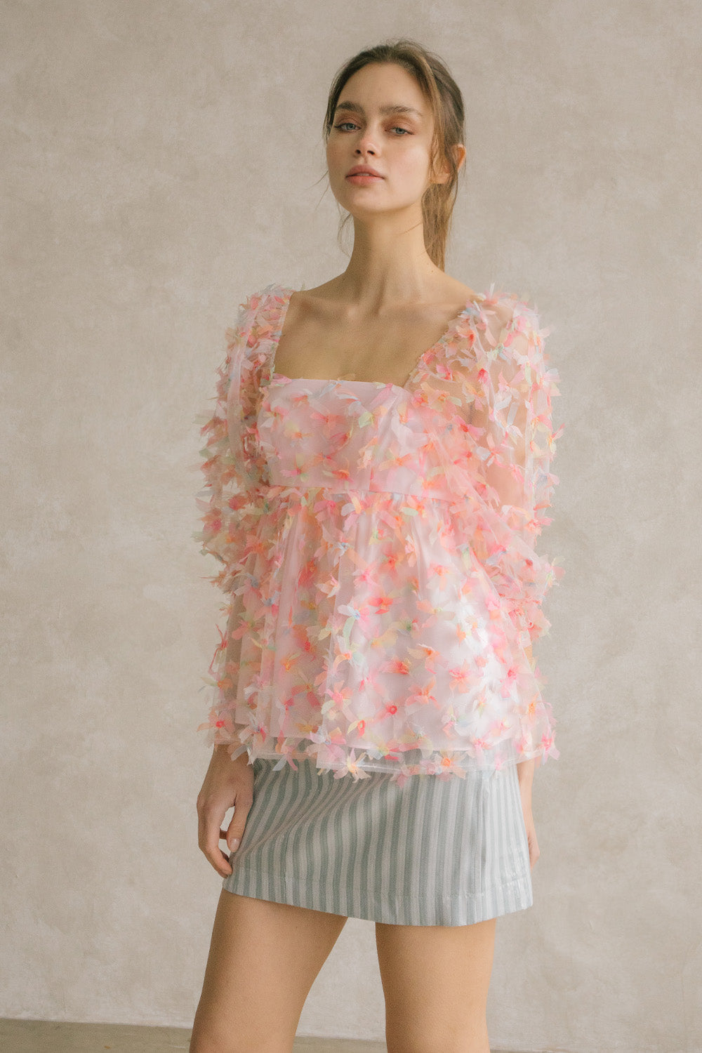 Woman wearing a pink tulle top with a blue striped skirt against a neutral wall.