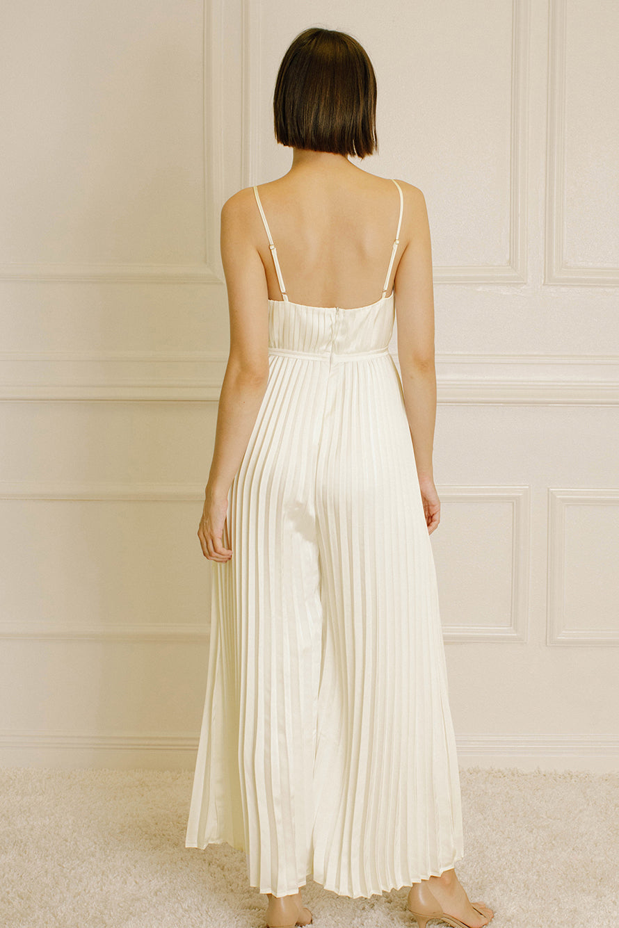 Back of a woman wearing an ivory pleated jumpsuit against a neutral wall.