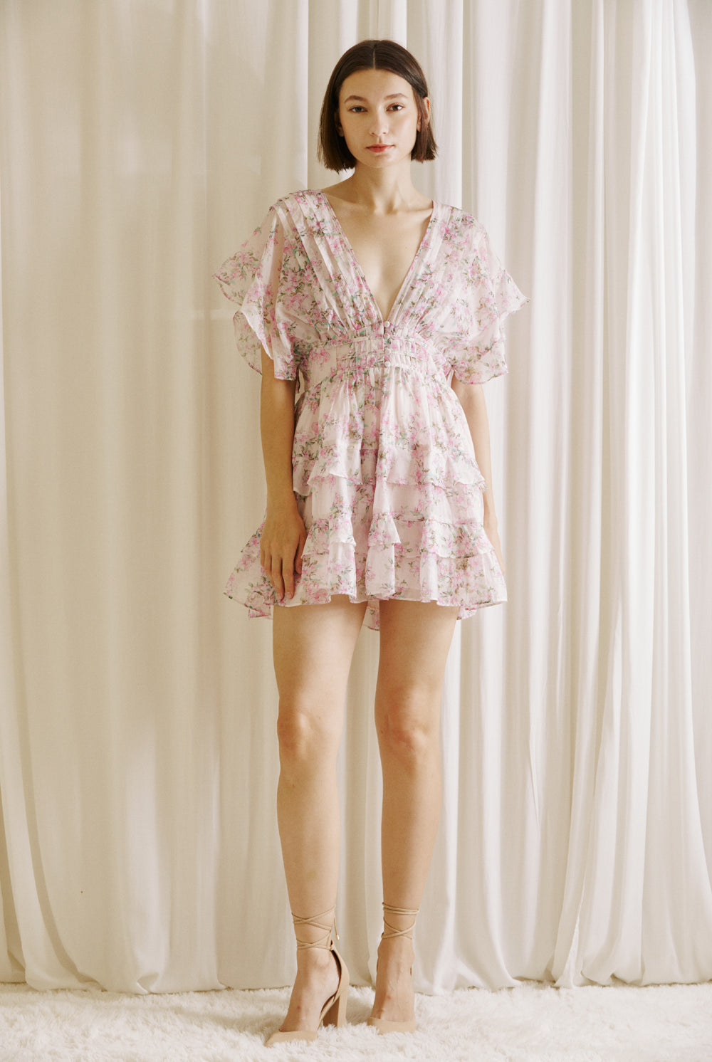 Woman wearing a pink floral dress and beige heels against a neutral background