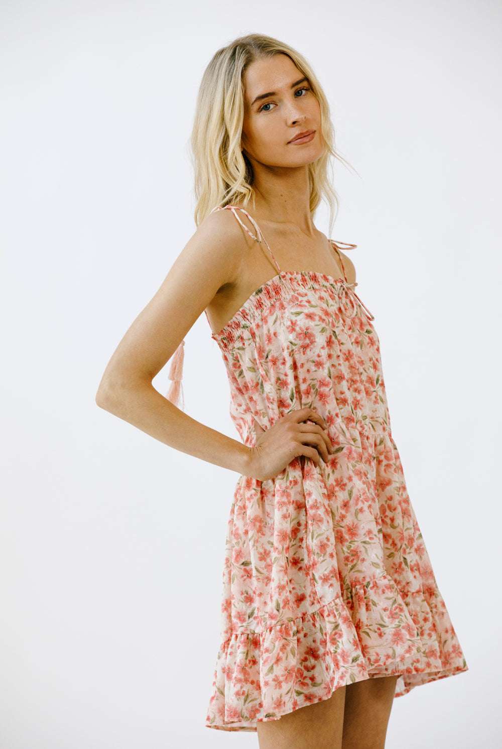 Side view of a woman wearing a vibrant pink floral print mini dress on a white background