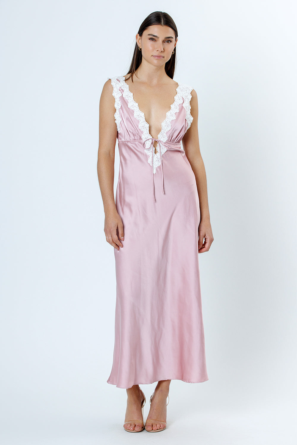 Woman wearing a pink satin nightgown with lace details on a white background