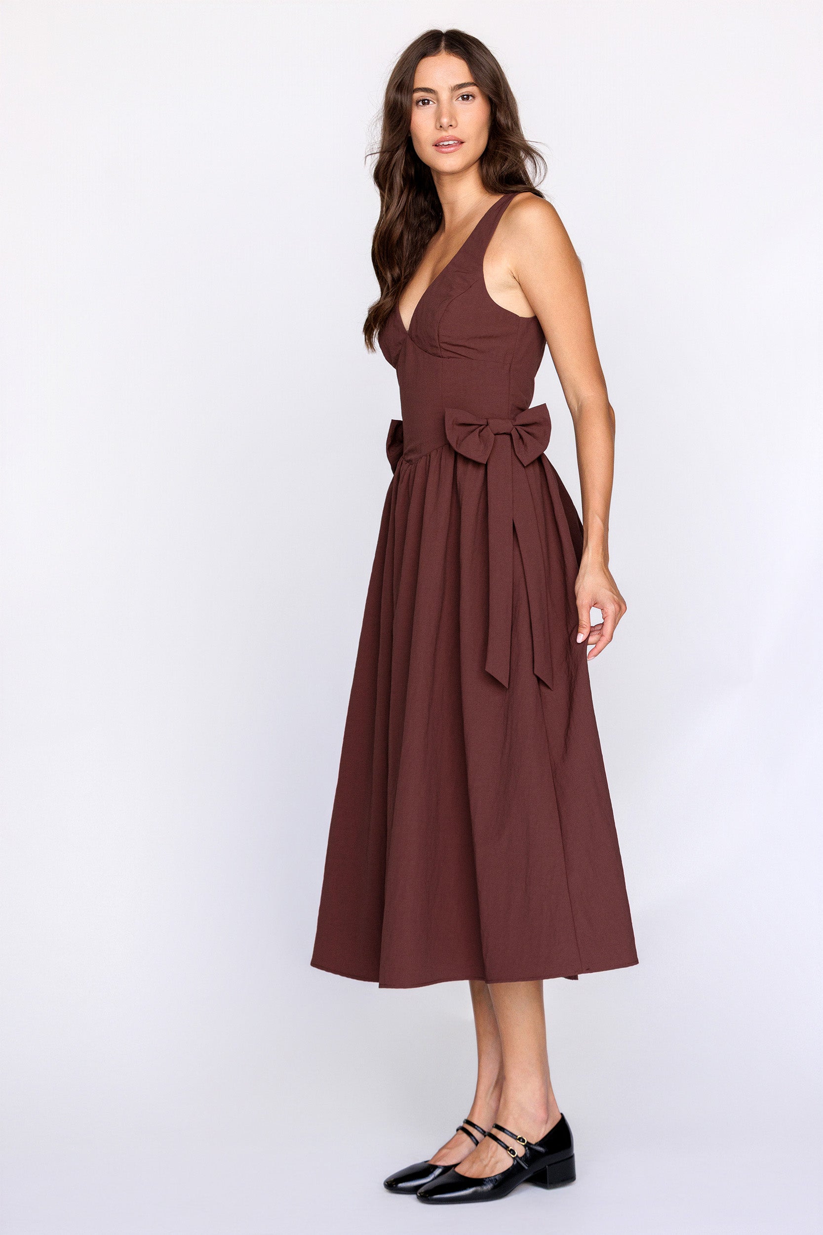 Side view of a woman wearing a brown dress with a bow detail on a white background