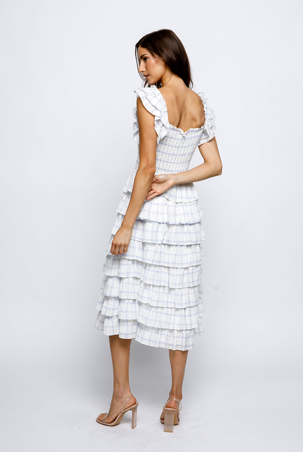 Woman wearing a white checkered dress with ruffled sleeves on a white background.
