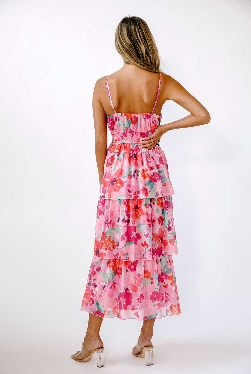 Back view of a model wearing a vibrant pink floral dress on a white background
