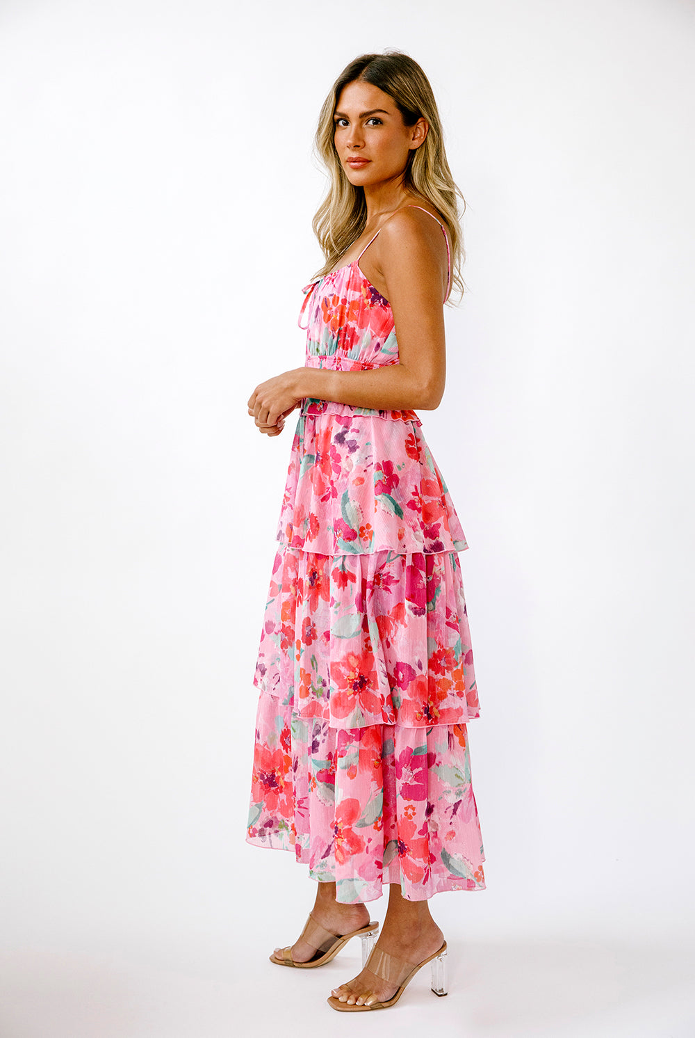 Side view of a woman wearing a vibrant pink floral dress on a white background