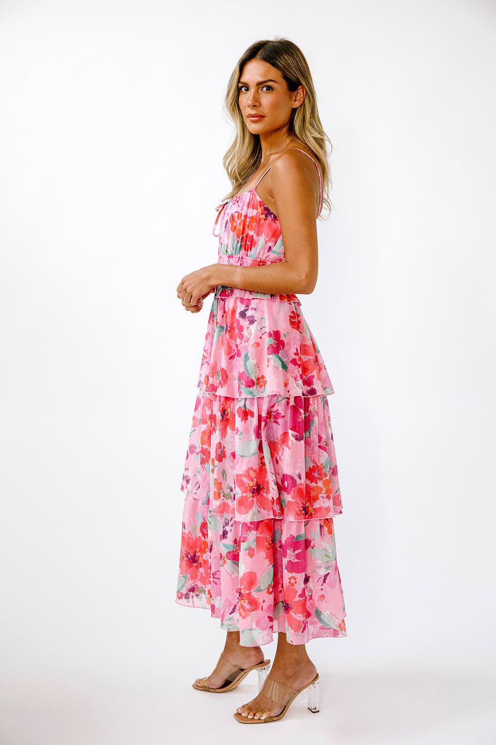 Side view of a woman wearing a vibrant pink floral dress on a white background