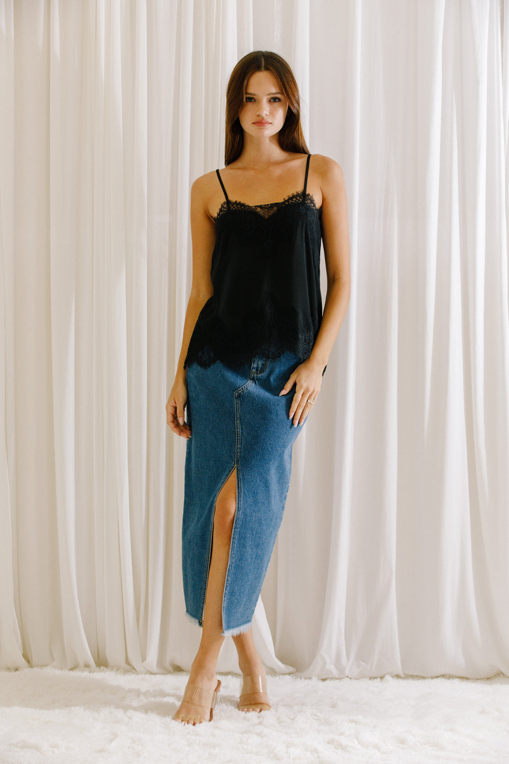 Woman wearing a black lace camisole and blue denim skirt against a white curtain background
