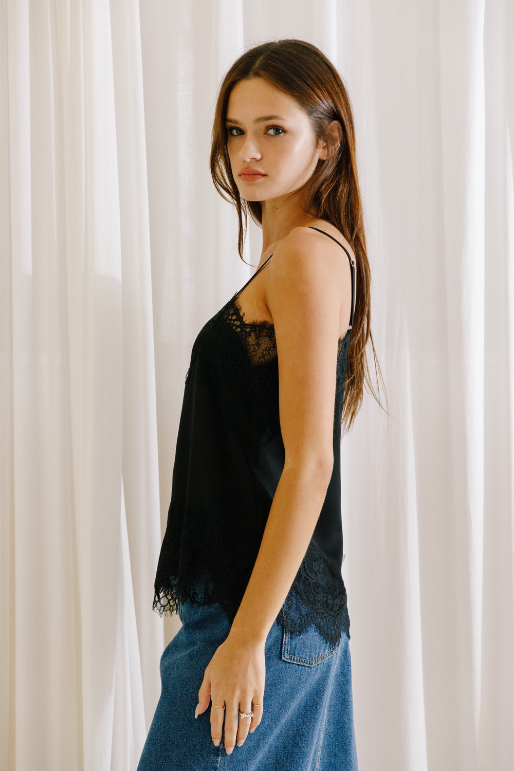 Side view of a model wearing a black camisole with lace trim and thin straps