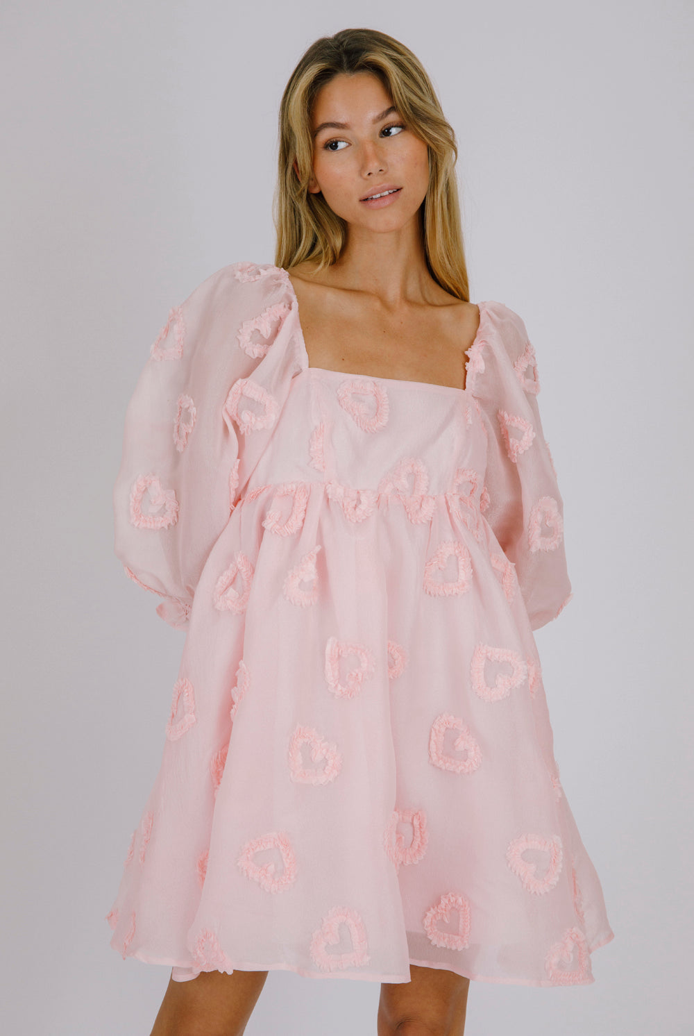 Woman wearing a pink dress with heart patterns on a plain background