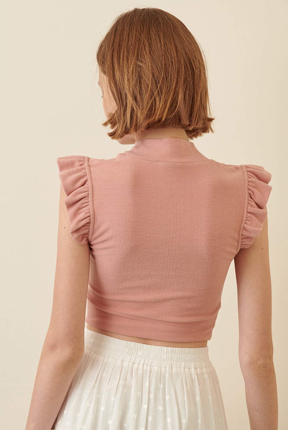 Back view of a woman wearing a pink ruffled top against a beige background
