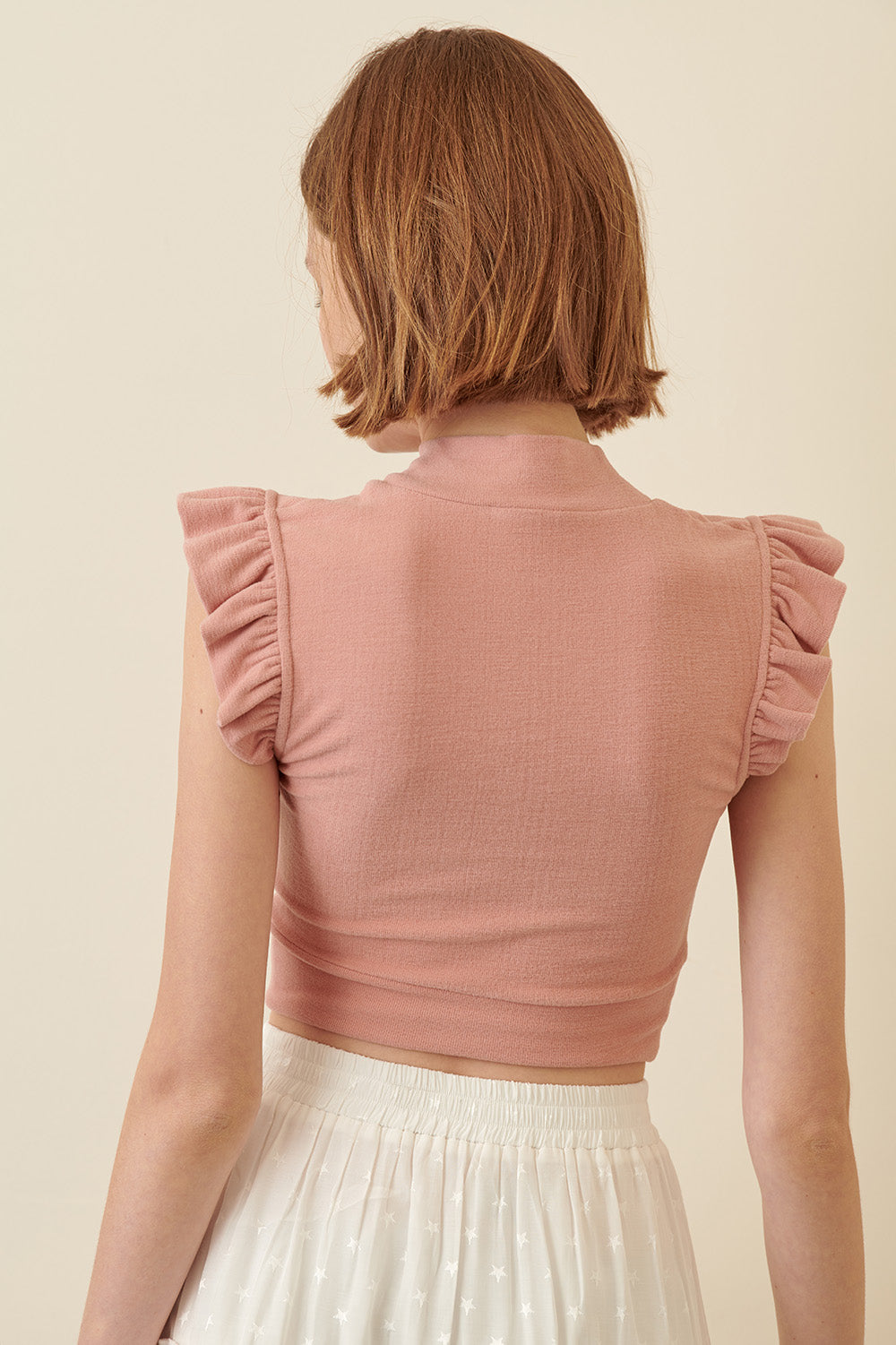 Back view of a woman wearing a pink ruffled top against a beige background