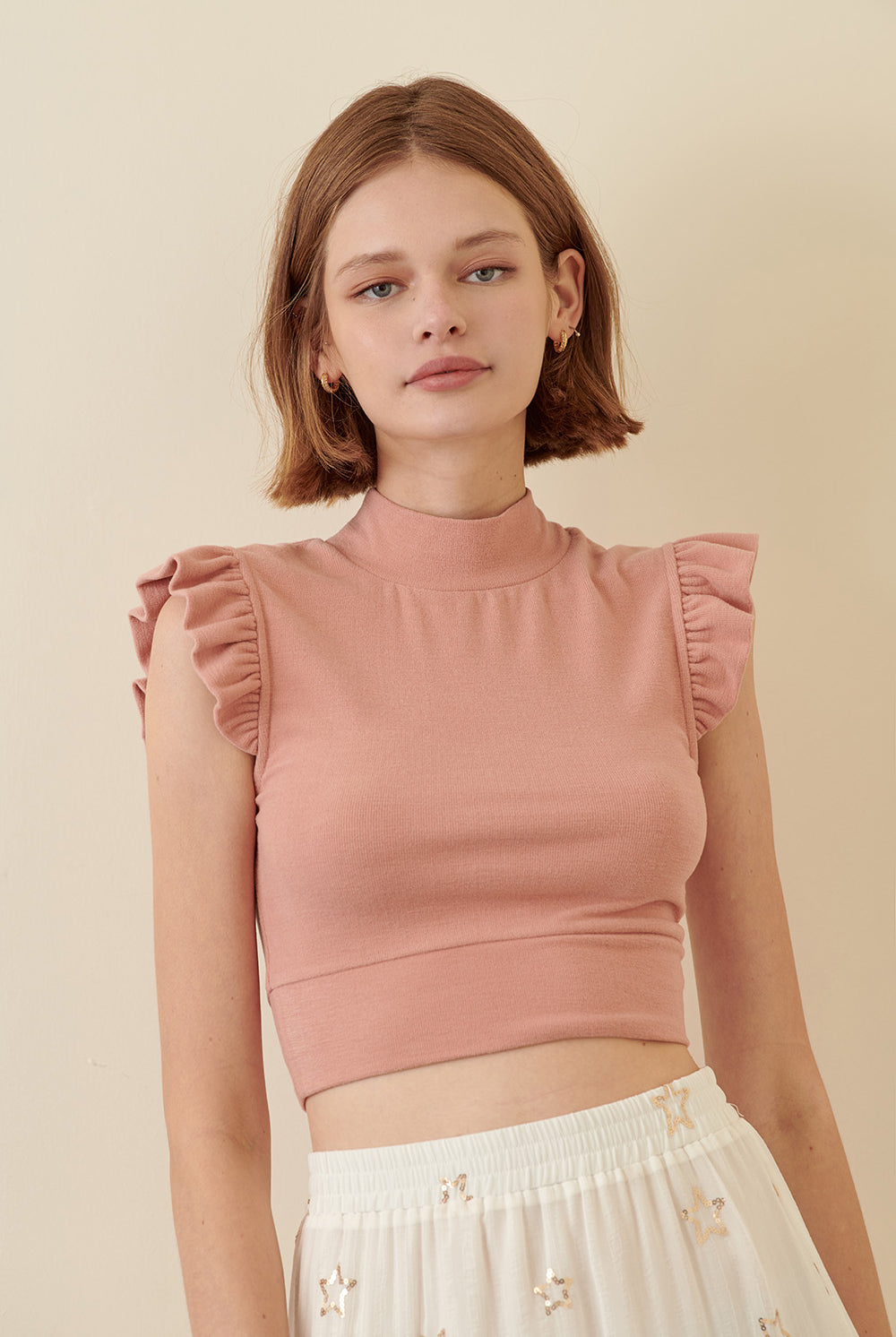 Woman wearing a pink top with ruffled sleeves against a beige background
