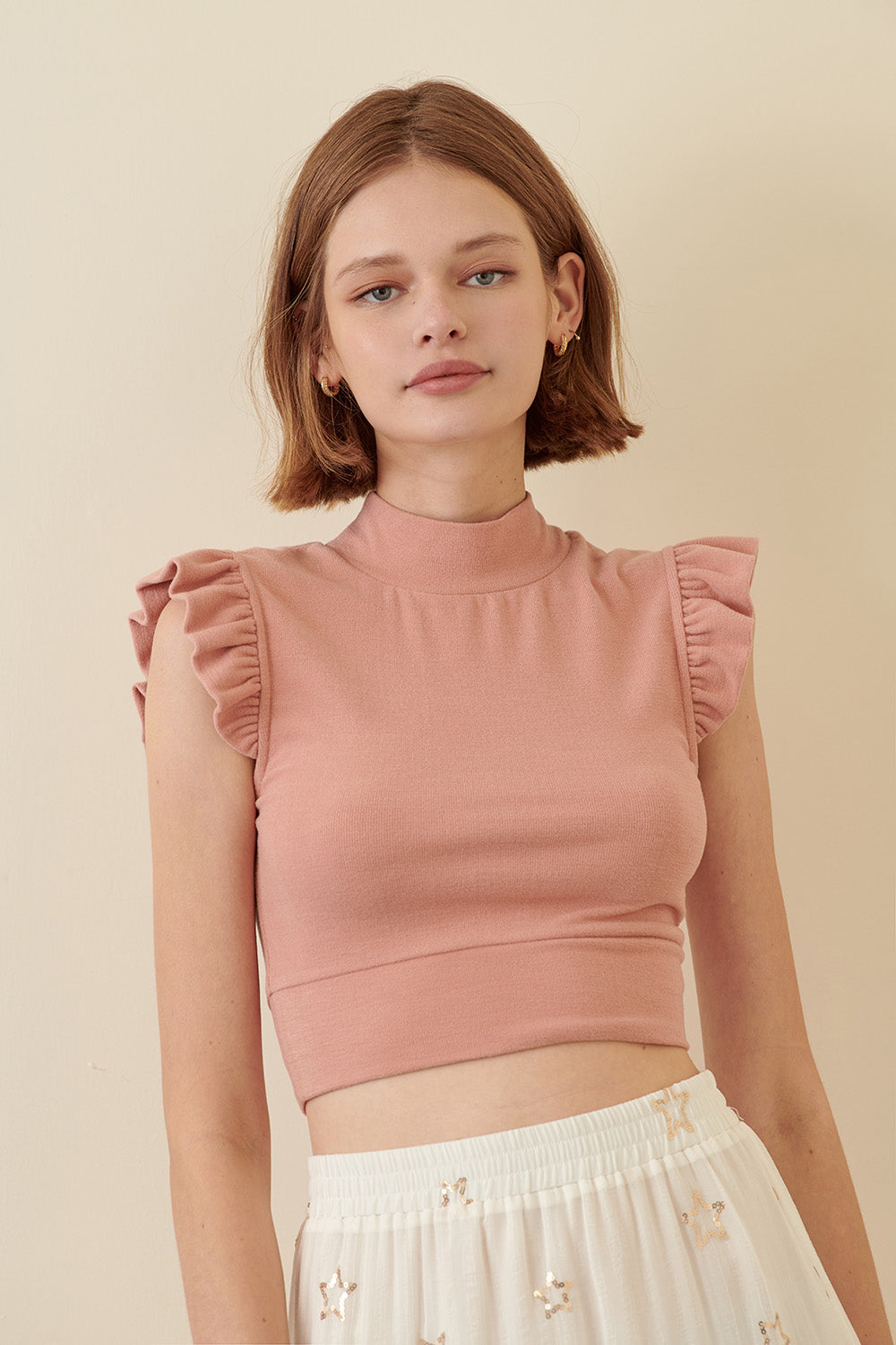 Woman wearing a pink top with ruffled sleeves against a beige background
