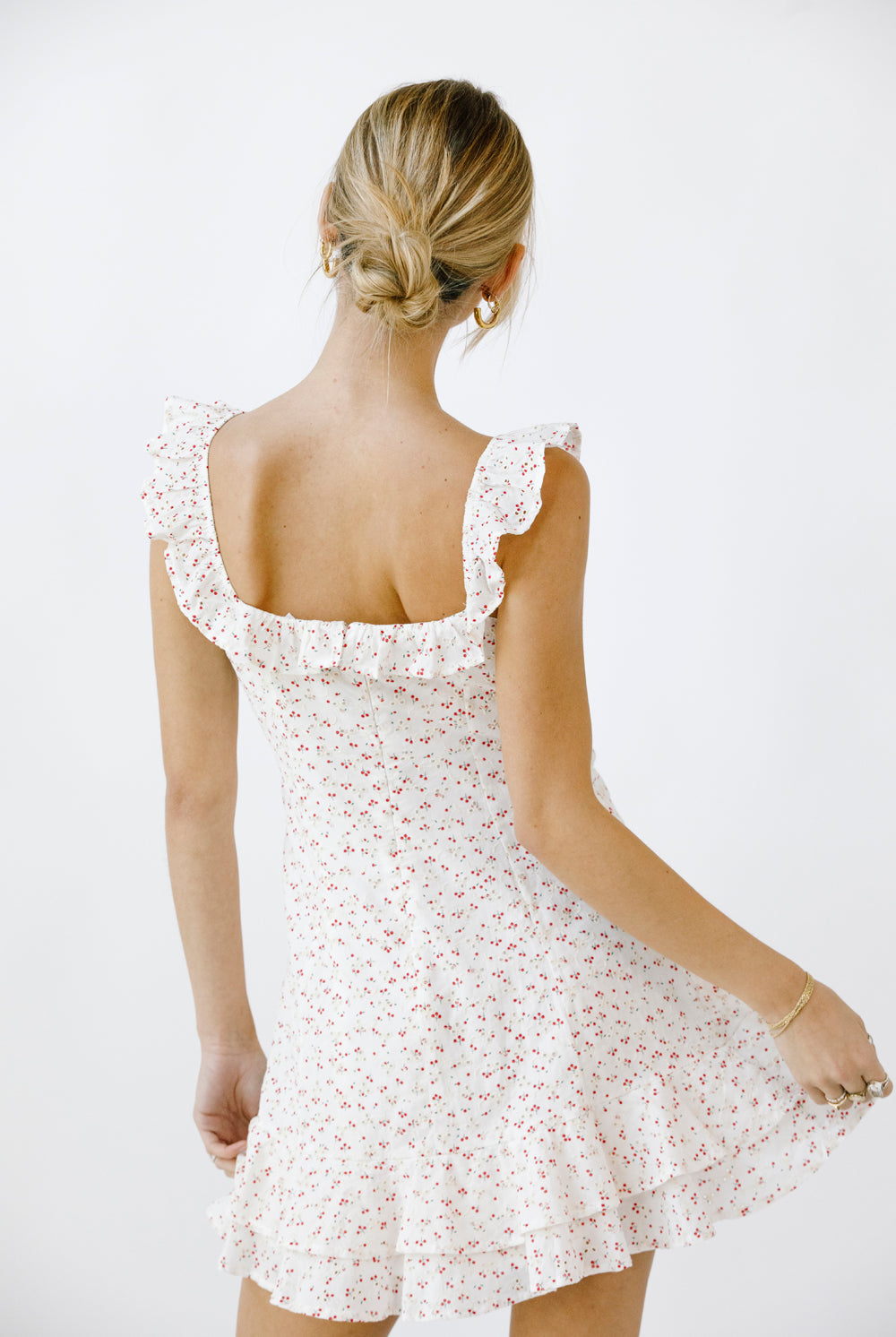 Back view of a woman wearing a white and red floral dress with a plain background