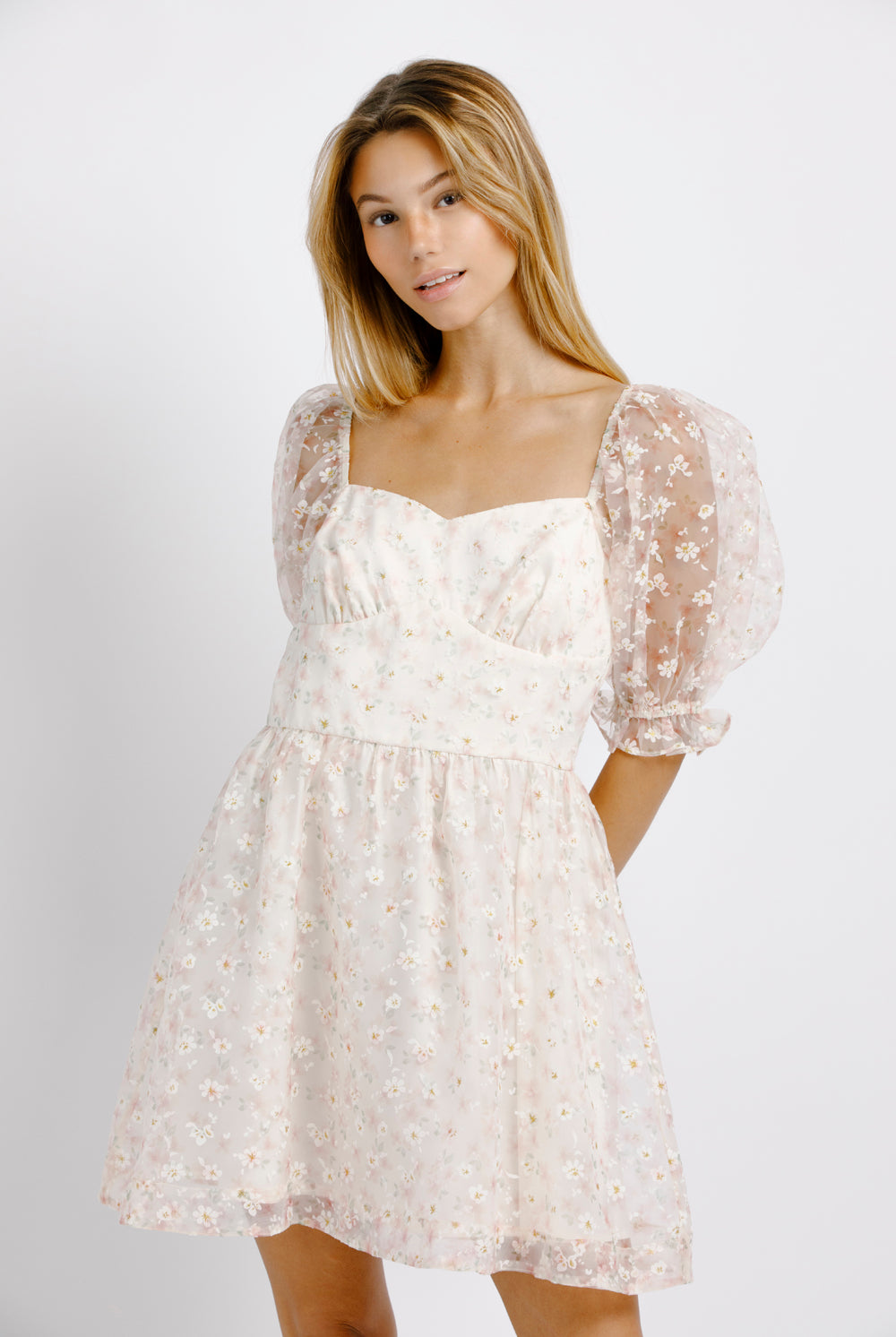 Woman wearing a cream dress with floral pattern and sheer puffy sleeves on a plain background