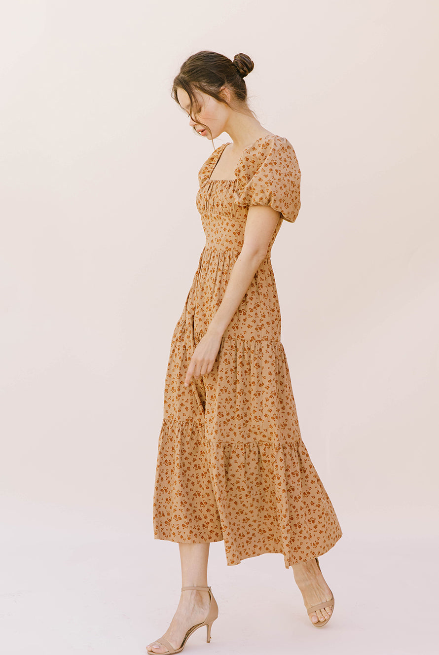 Side view of a woman wearing a brown floral midi dress on a plain background